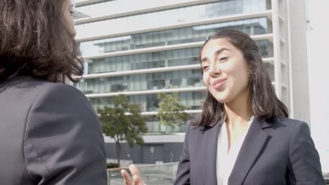 happy friendly business lady standing outside office building and talking to female colleague, listening and smiling