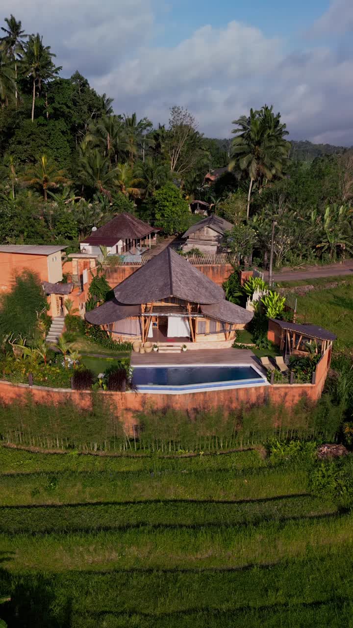 Vertical drone footage presents a serene bamboo villa in Bali, complete with poolside relaxation, lush greenery, and natural wooden design that blends seamlessly with the tropical landscape