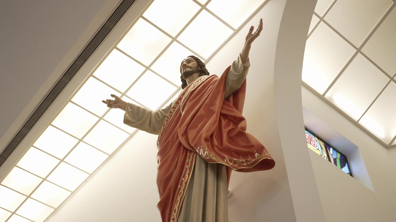 Statua di Gesù a braccia aperte sotto una luce soffusa all'interno di una chiesa moderna.