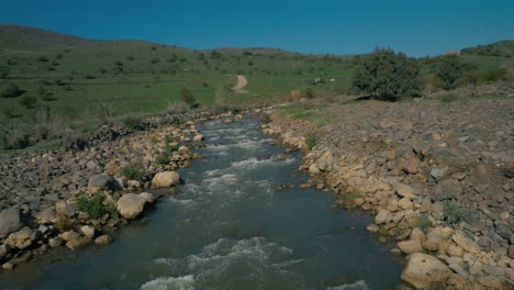 aerial, rocky flowing creek with green hillside in background, slow motion