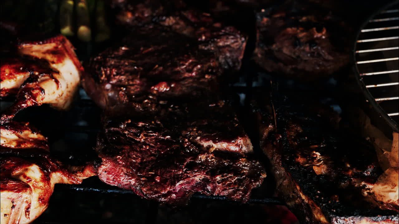 Close de carnes sendo preparadas em uma churrasqueira com batatas douradas, aspargos e alho