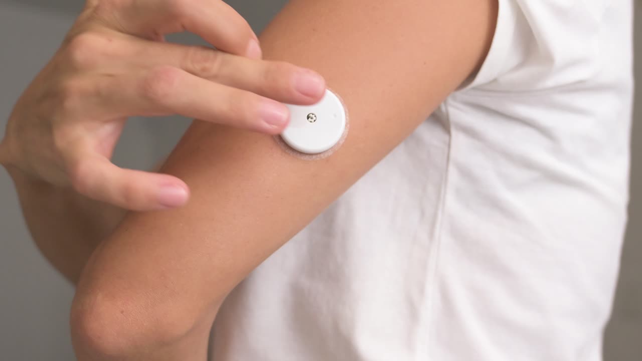 Close up of a woman applying a CGM sensor to her arm for diabetes management