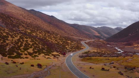 Campervan-drives-on-winding-road-with-deep-sloping-valleys-dotted-with-green-shrubs