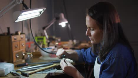 joyería caucásica centrada sentada en el escritorio, haciendo joyas en el taller