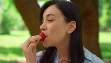 young woman eating strowberry on picnic close up. brunette bite fresh red berry.