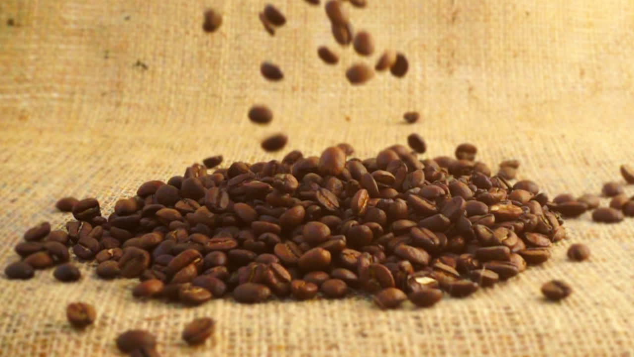 Chicchi di caffè cadono su tela di iuta al rallentatore.