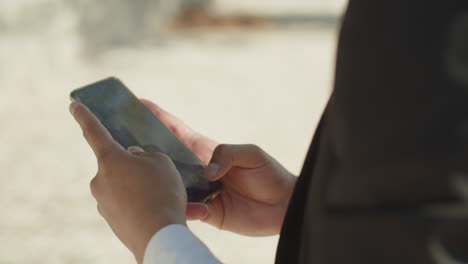 Close-up-of-young-mans-hands-swiping-smartphone-screen-outside.