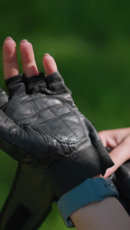 primer plano de la mano del individuo desabrochando la correa del guante de motociclista contra el telón de fondo de la vegetación exuberante, la mano está ajustando delicadamente el guante con enfoque en los dedos