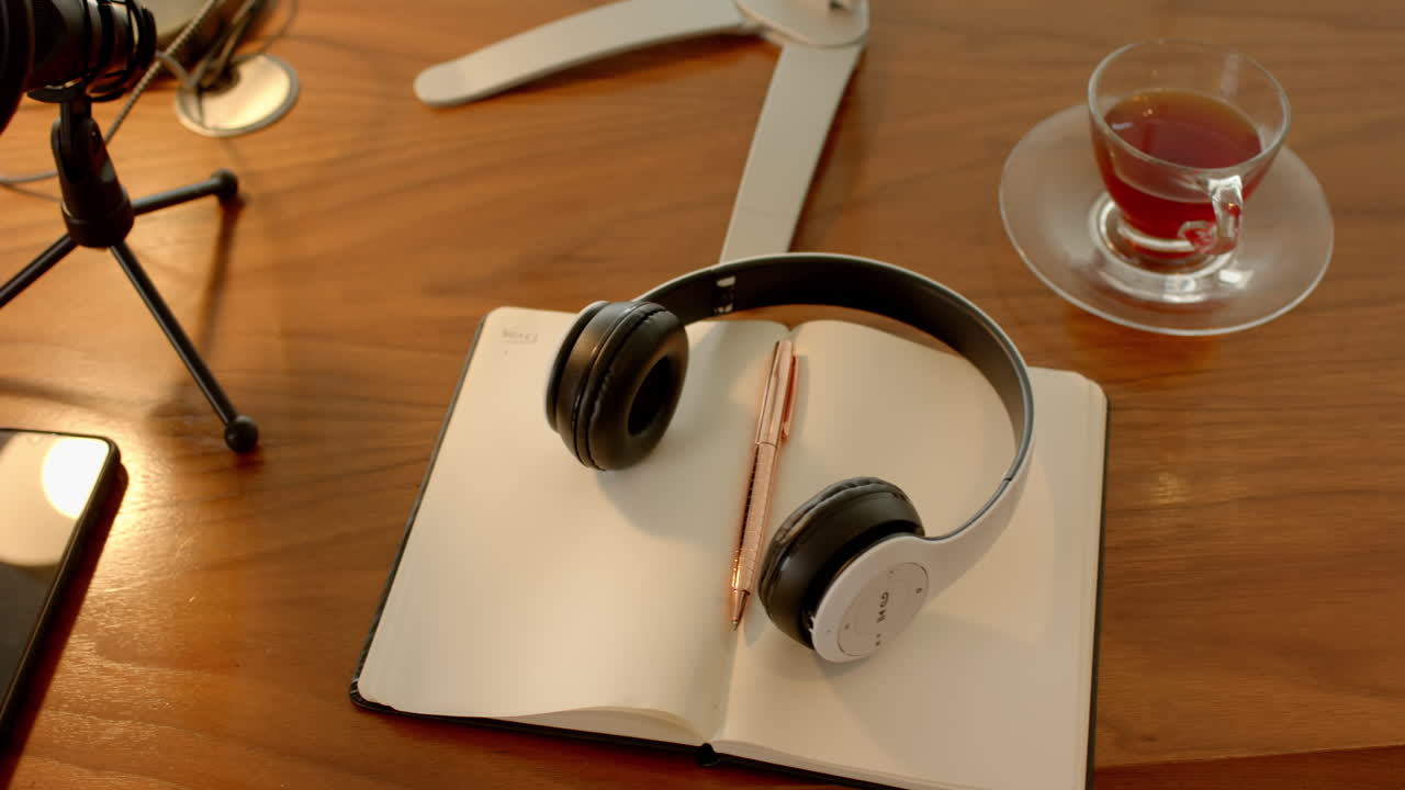 Headphones resting on open notebook with pen, smartphone, and tea on table, at home