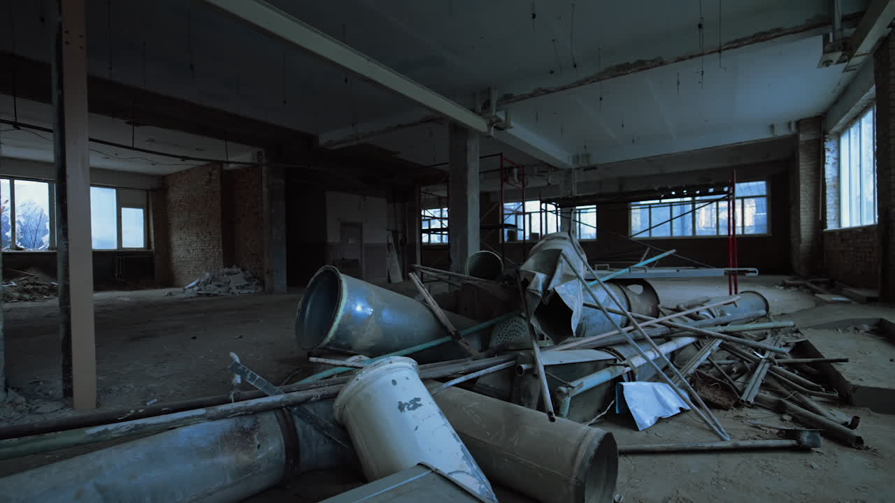Old pipes of diverse diameter lying on the floor of a big premise with columns inside. Being inside the building under construction or demolition.