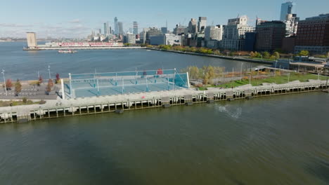 Fly-over-sport-playgrounds-on-piers-in-Hudson-river.-Tall-buildings-and-busy-road-on-waterfront.-Manhattan,-New-York-City,-USA