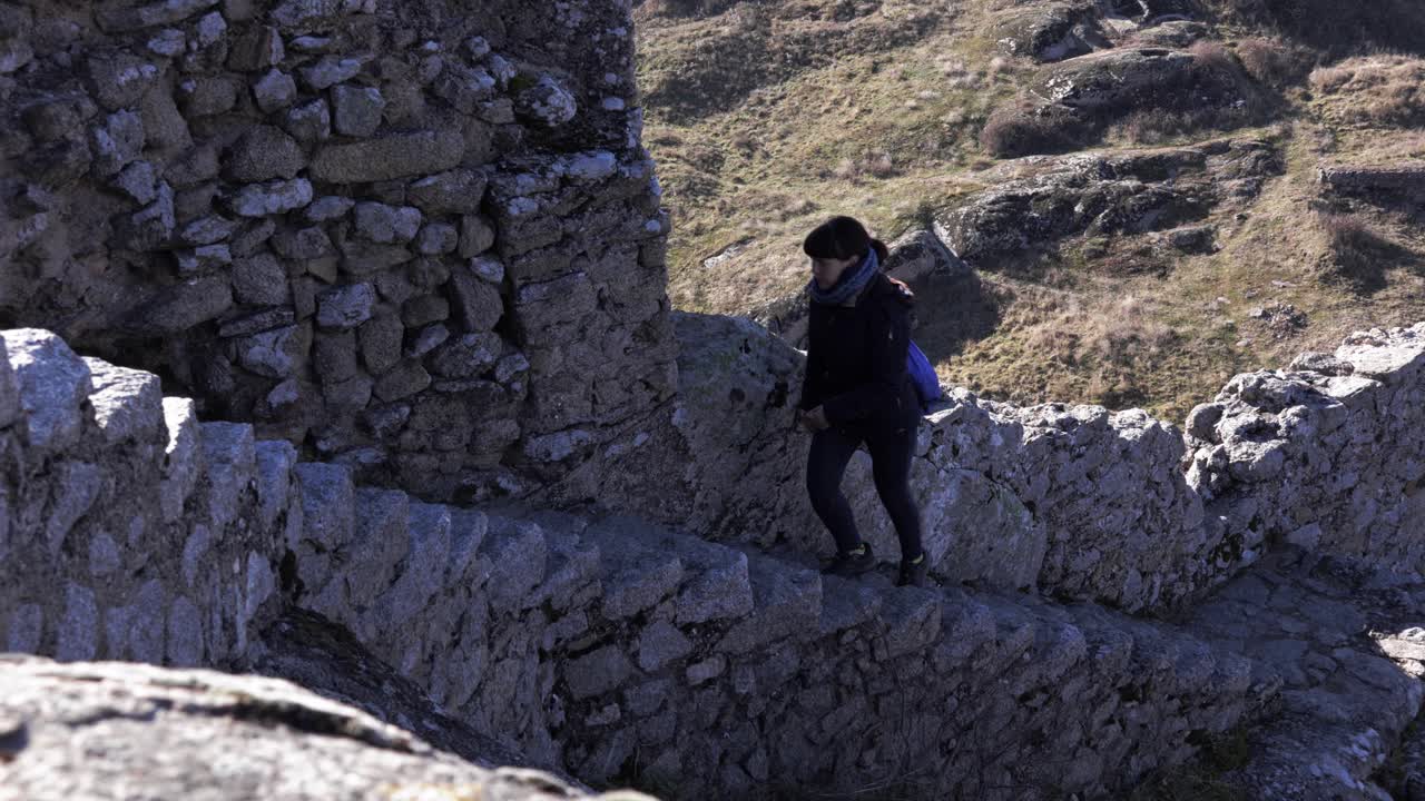 una chica con ropa de invierno subiendo escaleras rocosas desde un antiguo fuerte