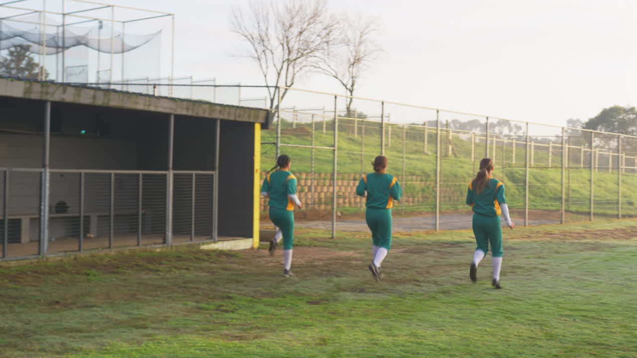 Multiracial female baseball players warming up, doing sidestepping and running on a pitch