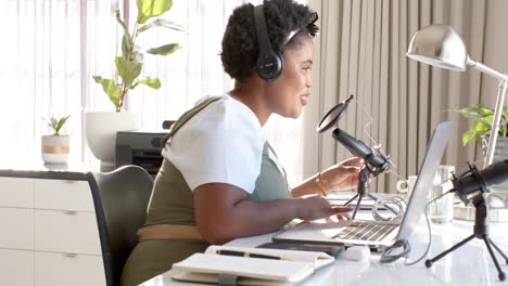 african american woman with headphones speaks into a microphone at home, recording a podcast