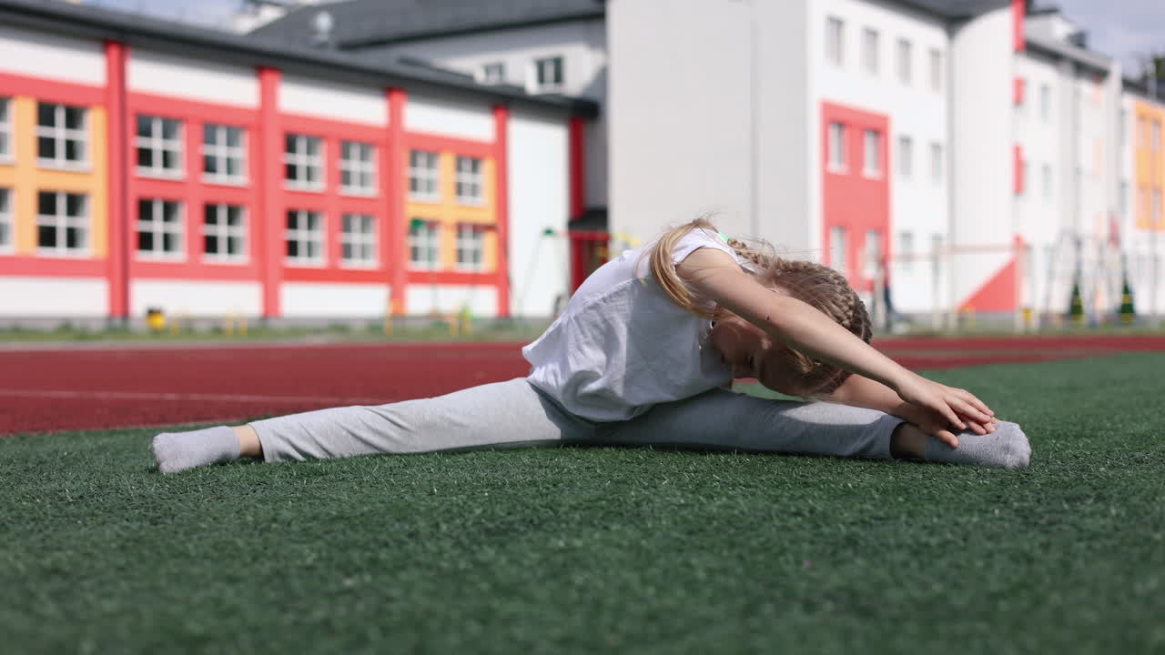 Ein kleines Mädchen treibt Sport auf dem Sportplatz. Ein Kind spielt draußen. Ein stylisches Mädchen in einem weißen T-Shirt. Ein Mädchen mit geflochtenen Haaren.