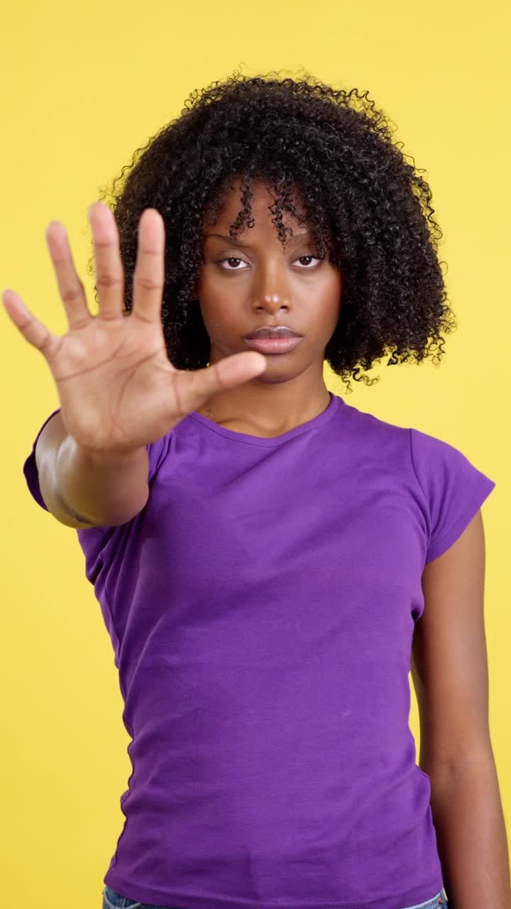 Young woman holding up hand in 'stop' gesture on yellow background