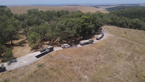 israel army infantry squad soldiers on vehicle driving through green field at training ground country road, aerial tracking shot