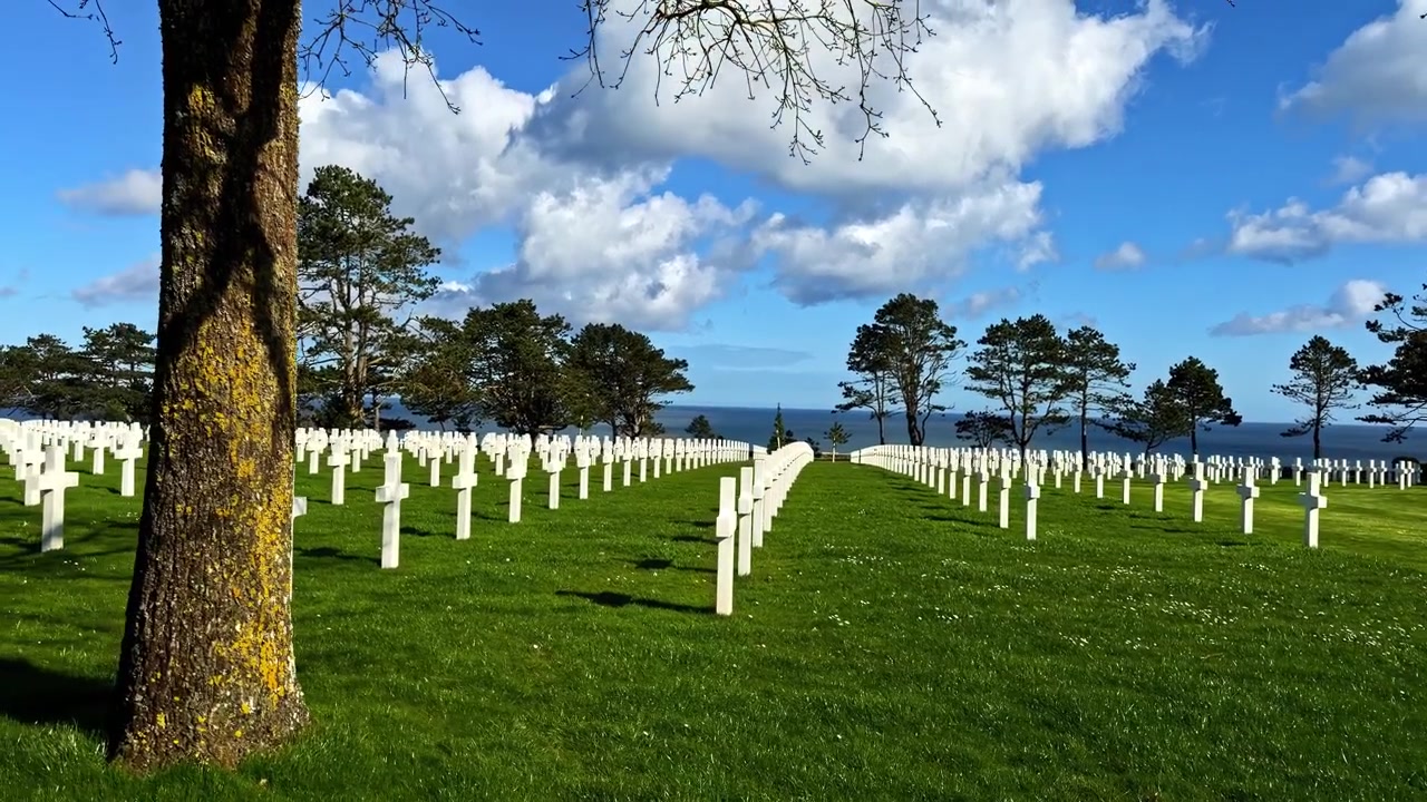 File di croci bianche allineate su un prato verde sotto un cielo blu nel cimitero della Normandia