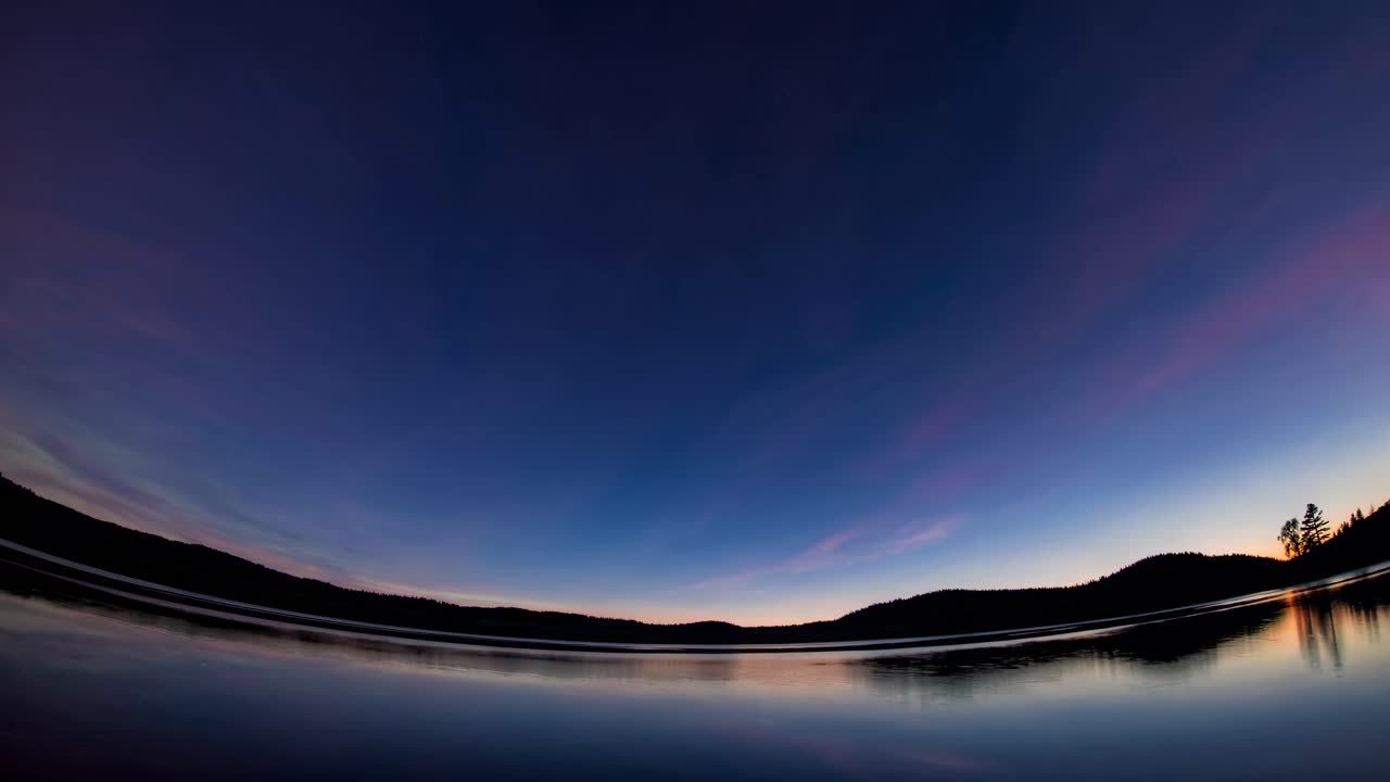 A serene sunset over a lake, captured with a fisheye lens. The wide-angle view enhances the horizon