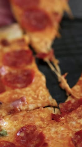 una mano toma una rebanada de pizza de pepperoni, mostrando queso pegajoso y un fondo rojo vibrante