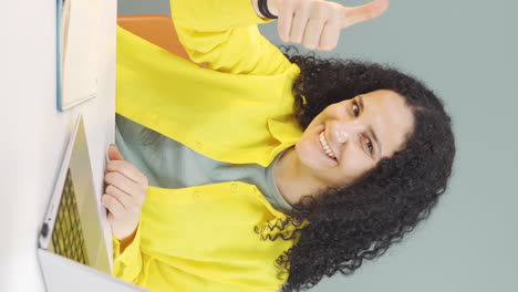 video vertical de una mujer joven mirando una computadora portátil haciendo un gesto positivo.