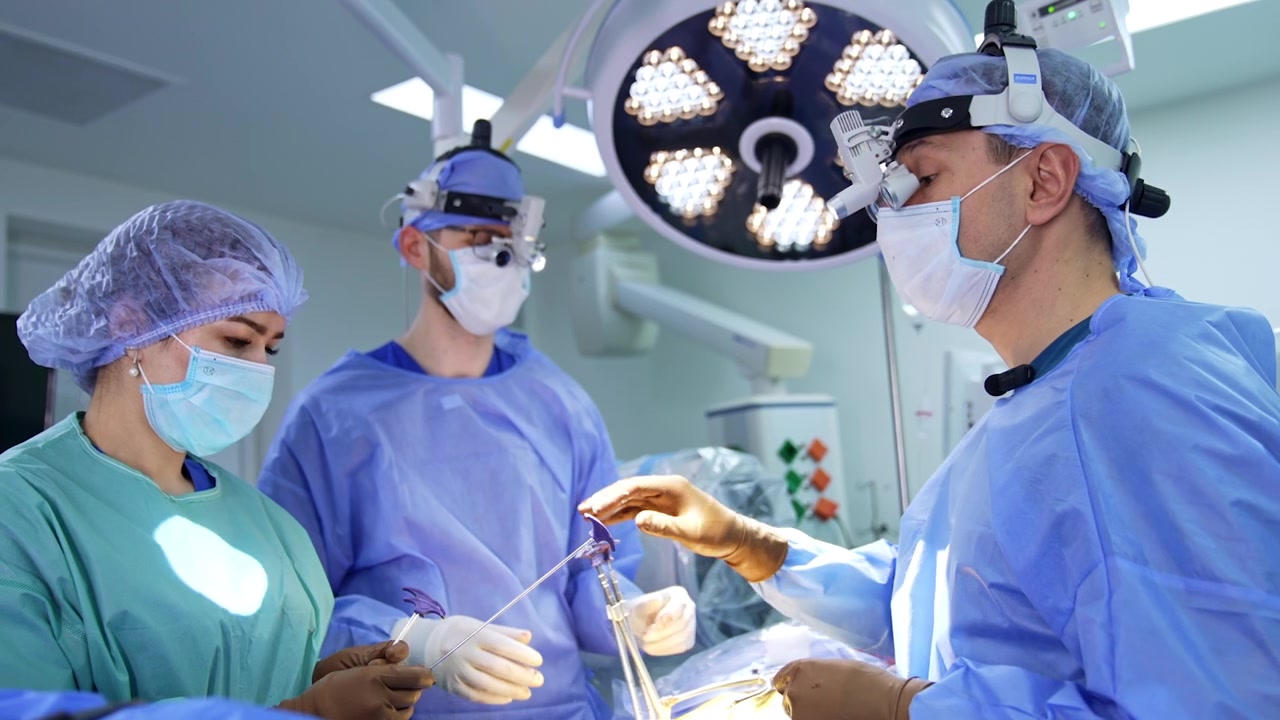 Neurocirurgião usando lupas cirúrgicas segura um instrumento de metal. Enfermeira assistente passa as ferramentas ao médico.