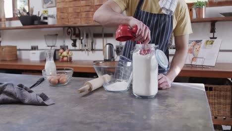 Midsection-of-caucasian-man-preparing-bread-dough-in-kitchen,-slow-motion