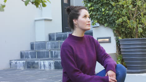 une femme blanche heureuse dans un pull violet assise devant la maison dans le jardin