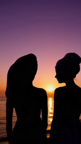 two women silhouetted against a vibrant sunset at the beach