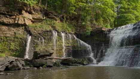 slow motion clip of waterfall flowing beside moss-covered rocks and trees on a sunny day