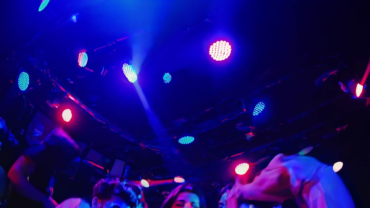 Ripresa video dinamica con un’angolazione bassa che cattura una vivace scena di festa con illuminazione rossa e blu intensa