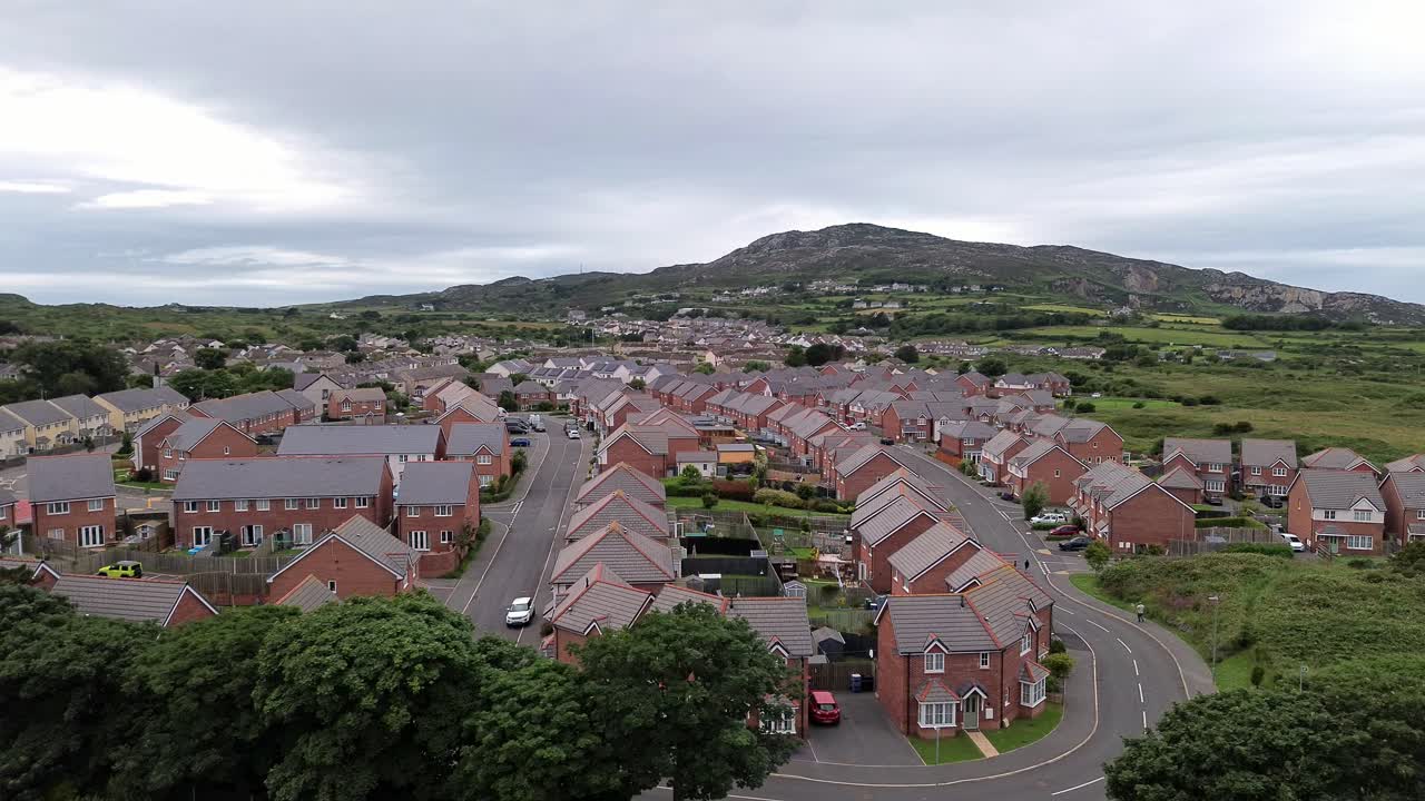 Aerial view flying across modern red brick housing neighbourhood under Holyhead mountain in Wales