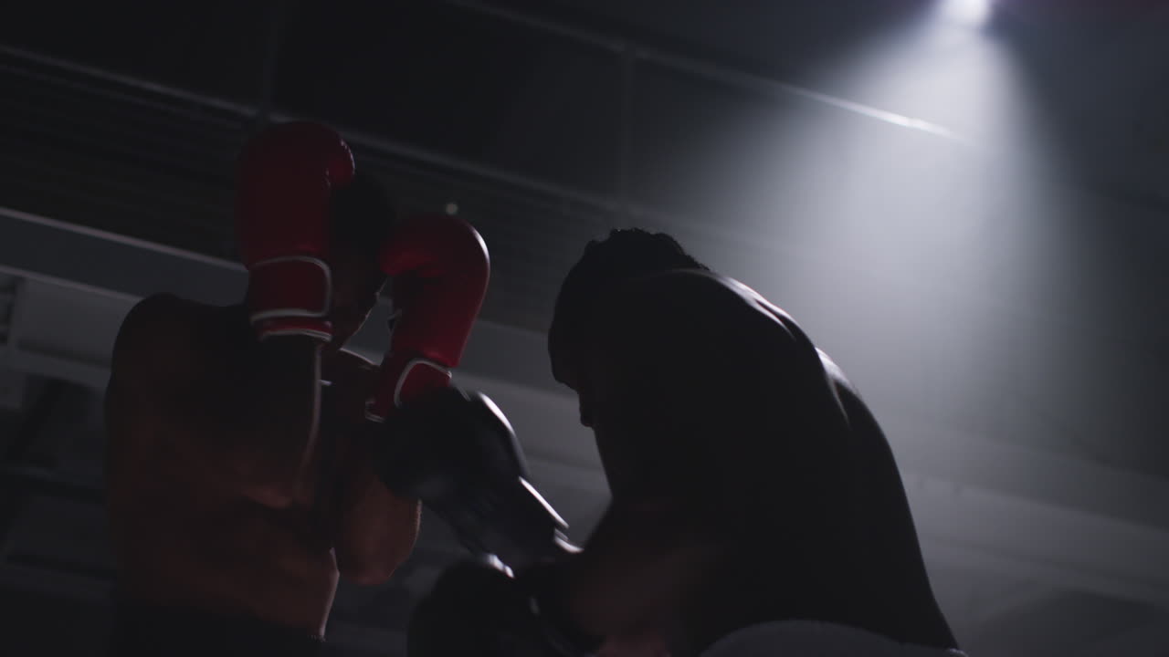 toma de cerca de dos boxeadores masculinos con guantes en el ring de boxeo luchando en un partido de boxe o con una iluminación de bajo nivel.