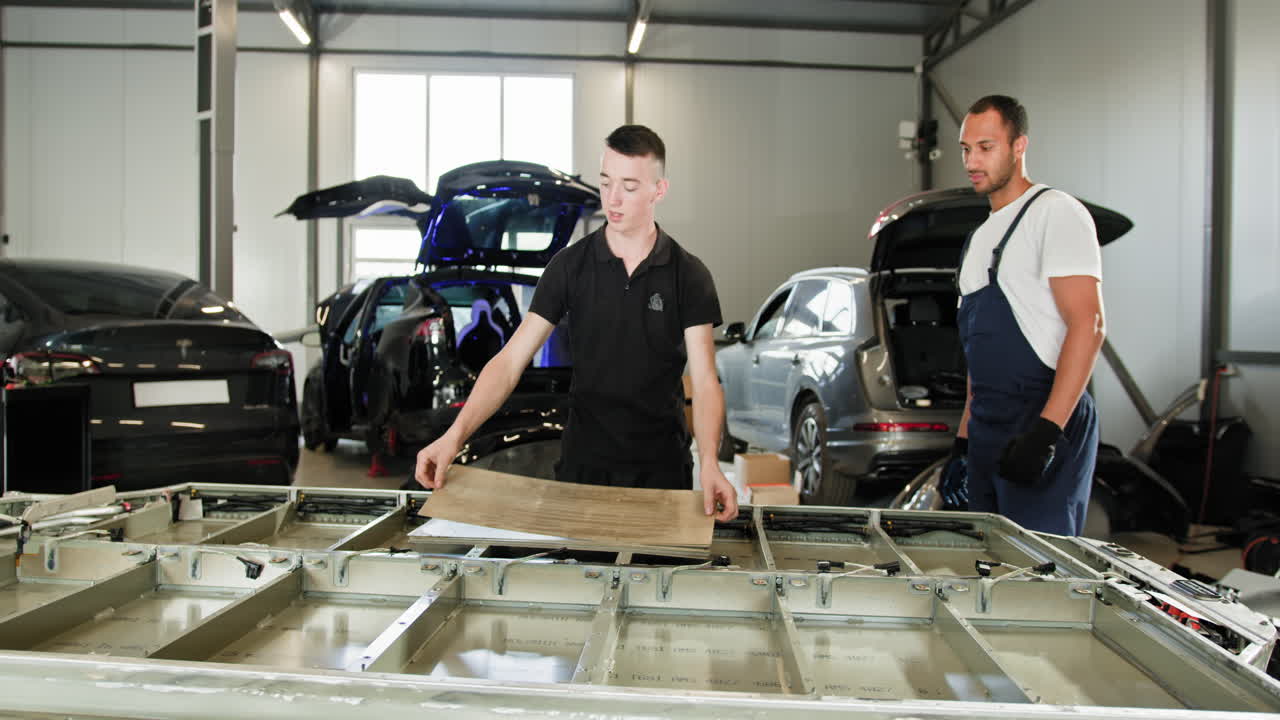 dos mecánicos trabajando en un vehículo eléctrico o una parte de una aeronave en un garaje