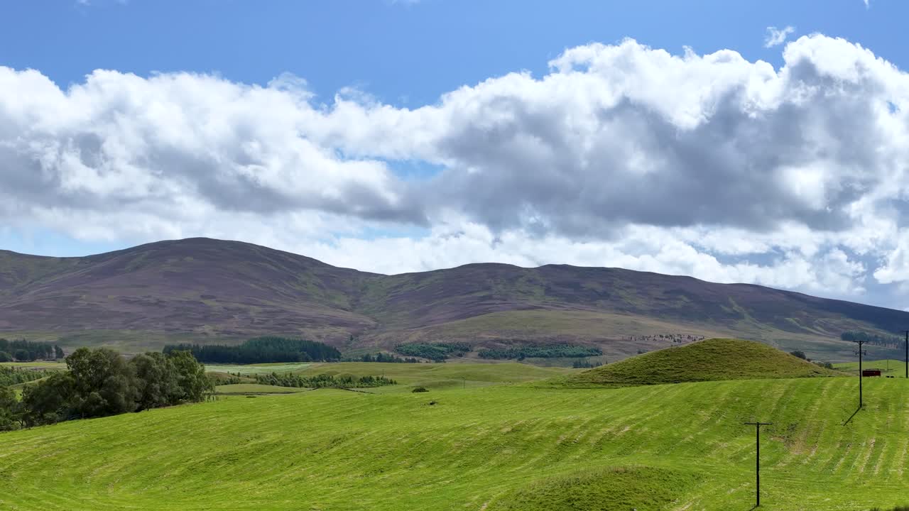 Camera glides along rural road, revealing green meadows, hills, winding river, and dramatic clouds