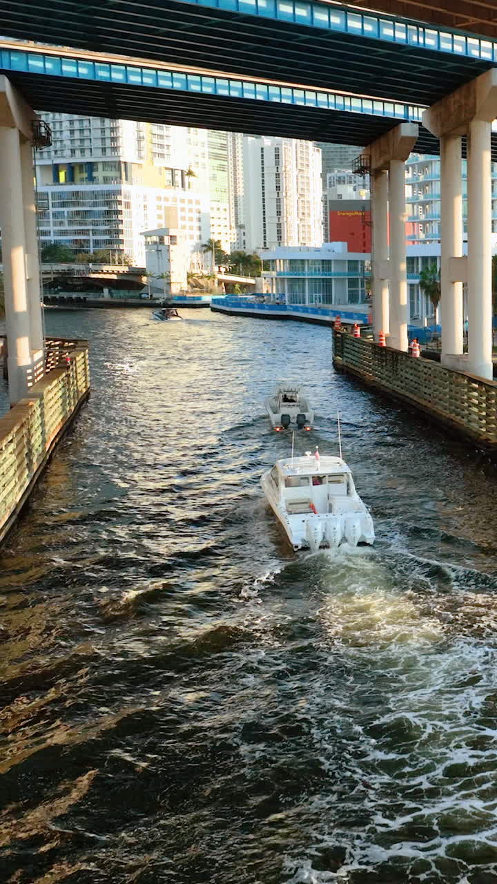 Miami, Florida, USA - January 05, 2024: Motorboat floats on river under highway bridge in downtown Miami. Aerial view. Drone flight over Miami river with bridges. Vertical video
