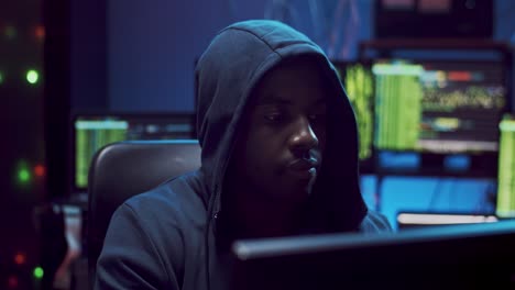 cận cảnh của điệp ảo nam trẻ tuổi trong một chiếc mũ trùm đầu hacking một số phần mềm vào ban đêm trong phòng tối 1
