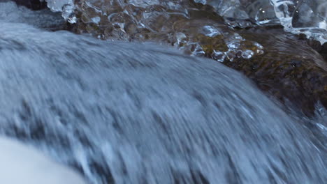 Toma-Detallada-Del-Agua-Del-Río-Que-Fluye-Durante-El-Invierno-Con-Carámbanos-En-El-Costado,-Vista-Panorámica-A-La-Derecha