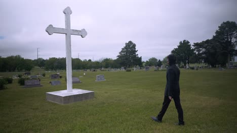 young, religious man in black suit worshipping and praying in front of christian cross