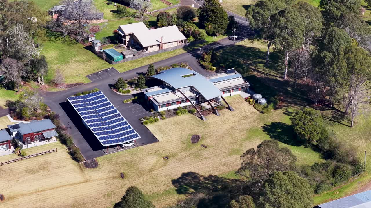 Drone ascends above rural buildings with solar panels, revealing green landscape and clear daylight