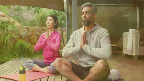 animation of light spots over diverse couple doing yoga and meditating on terrace