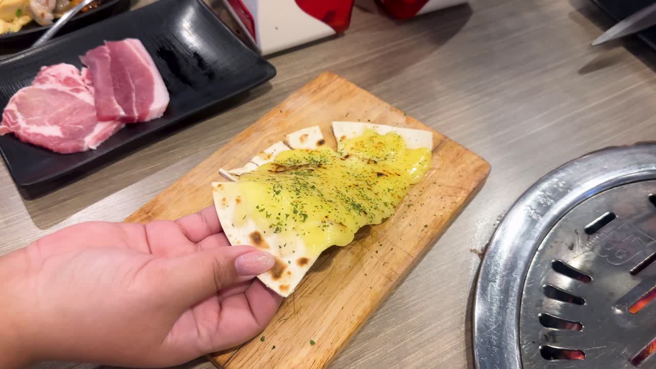 Hands prepare a Korean BBQ pizza with toppings on a wooden board in a well-lit Bangkok restaurant