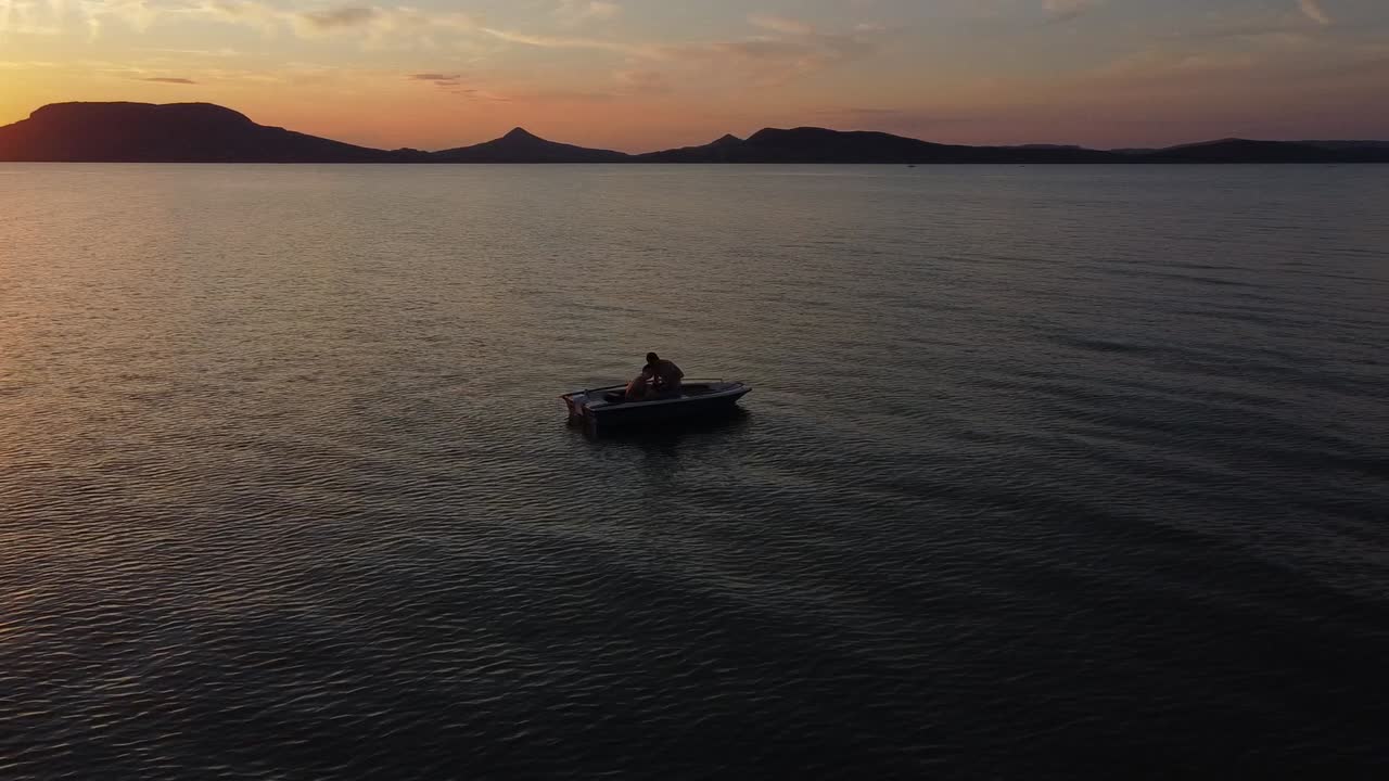 vista aérea de una pareja joven en un bote flotando en el lago al atardecer con montañas en el fondo