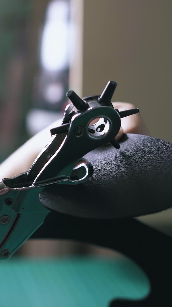 CU: Skilled person makes holes in black leather mask template with punch pliers in workshop close view