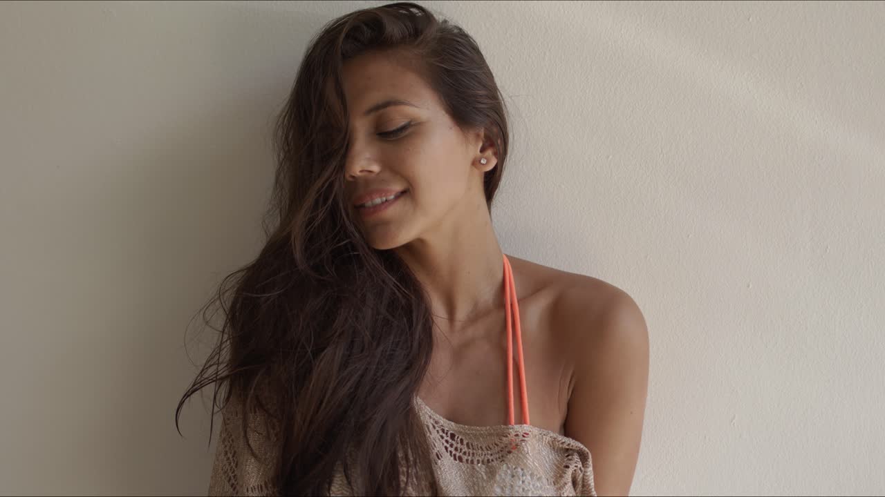 una morena de pelo largo de pie sobre un fondo blanco