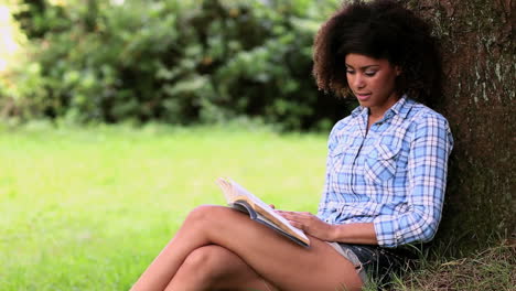 Beautiful-woman-reading-in-the-park-leaning-against-a-tree