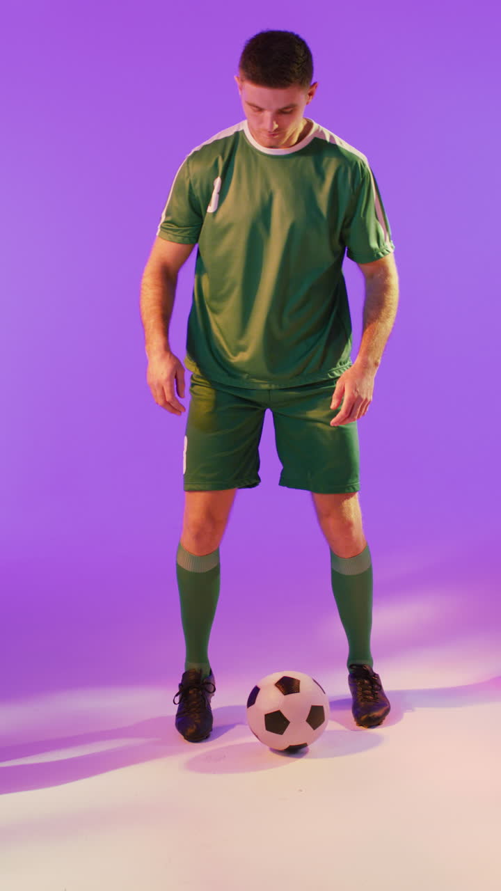 video verticale di un calciatore maschio caucasico con il calcio sopra l'illuminazione rosa al neon