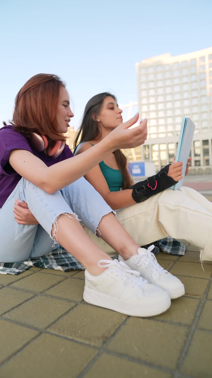 dos mujeres jóvenes sentadas al aire libre en un entorno urbano.