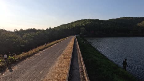 person walking on dam path by a lake