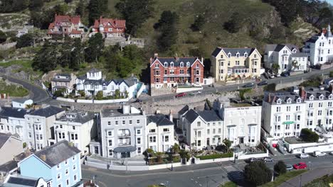 Colourful-Llandudno-seaside-holiday-town-hotels-against-Great-Orme-mountain-aerial-view-right-orbit-slow-shot